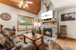 A cozy living room with a stone fireplace, a mounted deer head, a clock, and a television displaying 'RENTBRJONSON.COM'.
