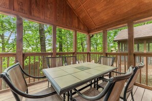 Eine überdachte Terrasse im Freien mit Tisch und Stühlen, umgeben von Holzbalkonen und Bäumen.