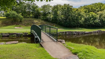 A green bridge over a pond with a golf course in the background.