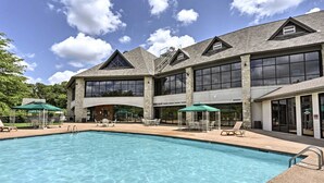 A large outdoor swimming pool with lounge chairs and umbrellas, surrounded by a building with large windows and stone pillars. - Romantic Getaway Near Silver Dollar City with Free Tickets & Onsite Golf Course (Reeds Spring)