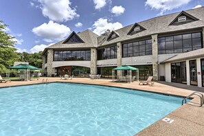 A large outdoor swimming pool with lounge chairs and umbrellas, surrounded by a building with large windows and stone pillars. - Romantic Getaway Near Silver Dollar City with Free Tickets & Onsite Golf Course (Reeds Spring)