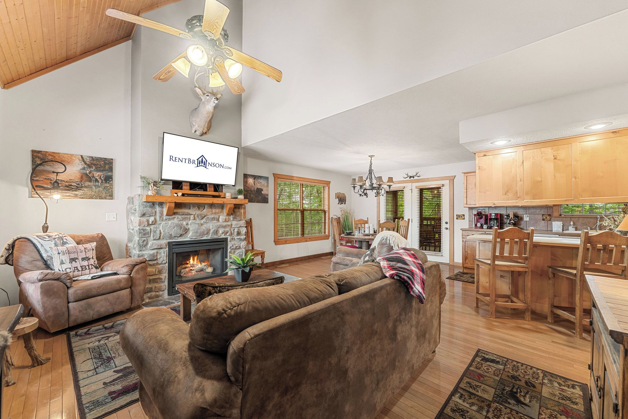 A spacious living room with a fireplace, a television mounted on the wall, and a dining area with wooden furniture.