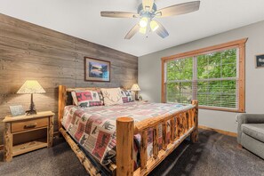 A bedroom with a wooden bed, a nightstand, a lamp, a window with blinds, and a ceiling fan. - Romantic Getaway Near Silver Dollar City with Free Tickets & Onsite Golf Course (Reeds Spring)
