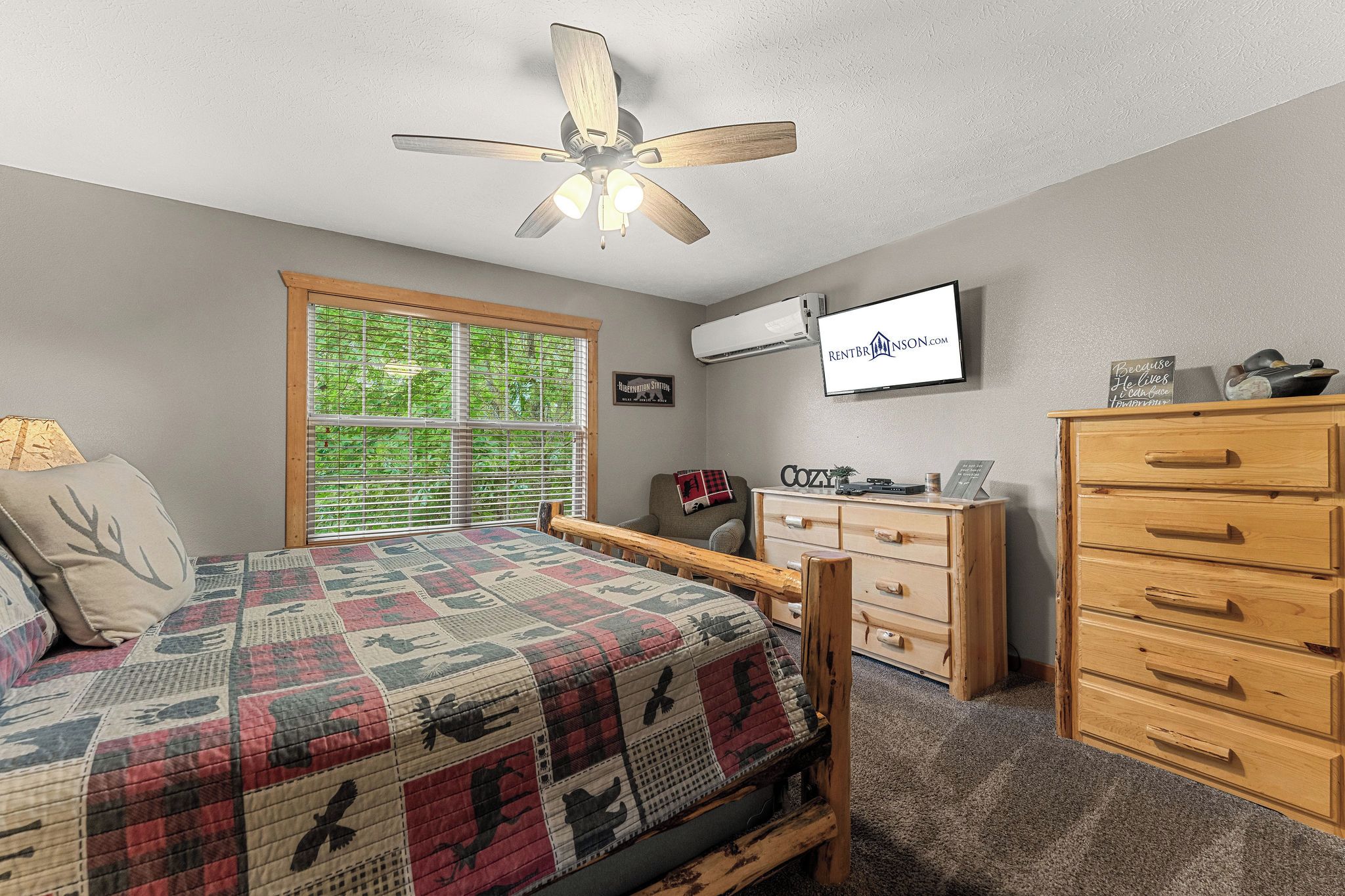 A bedroom with a bed, a wooden dresser, a television, and a ceiling fan.
