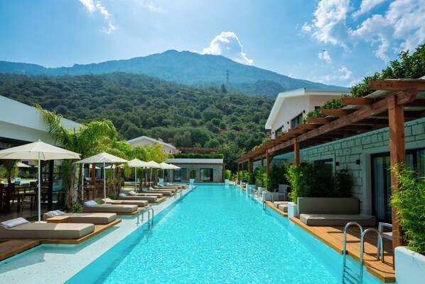 A swimming pool with lounge chairs and umbrellas, surrounded by greenery and a mountain view. - The Pearl Ölüdeniz (Fethiye)