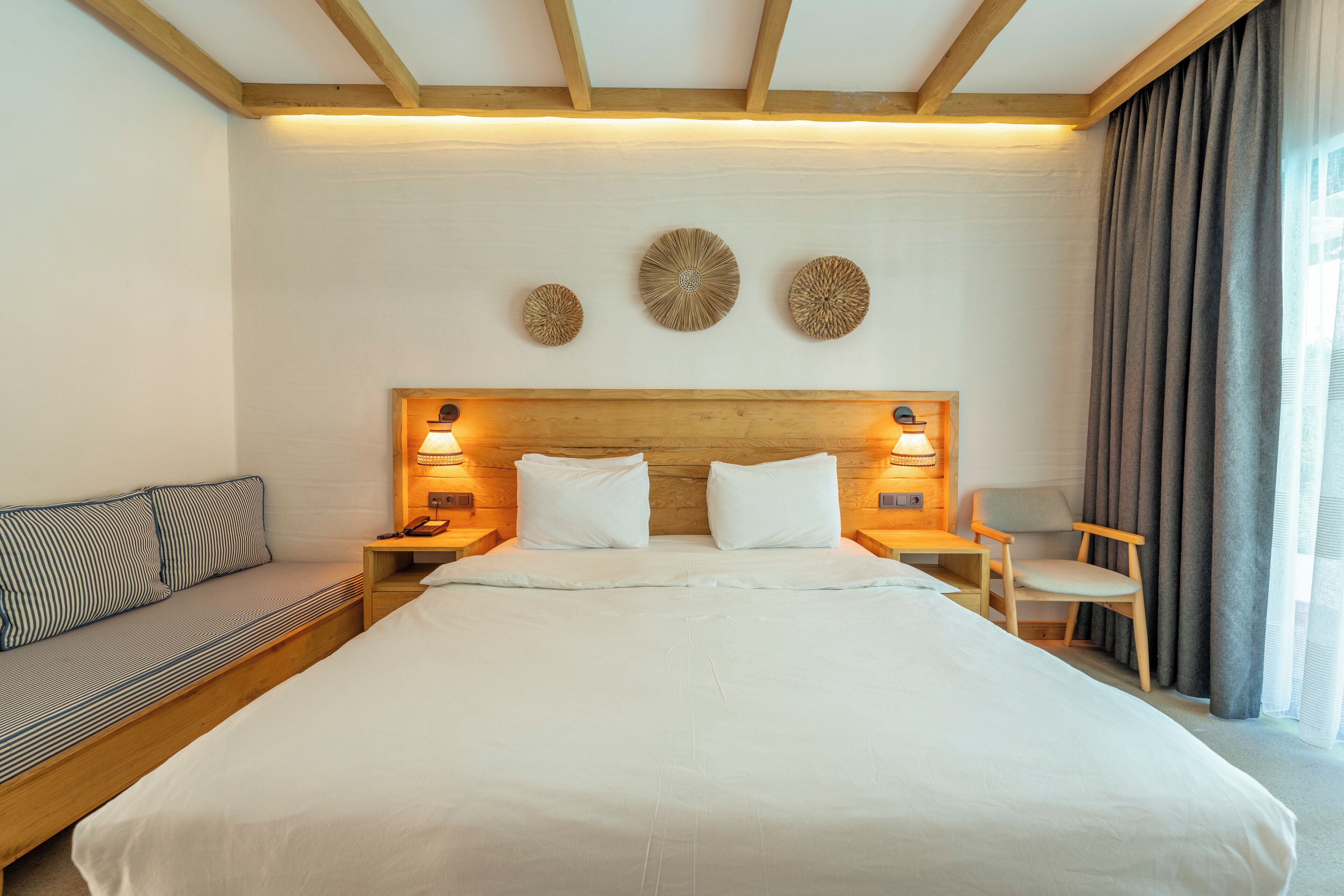 A hotel room with a large bed, a wooden headboard, bedside lamps, a sofa, and a chair.