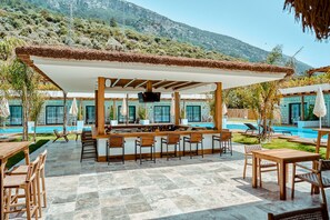 An outdoor bar area with a pool, wooden furniture, and a mountain backdrop. - The Pearl Ölüdeniz (Fethiye)