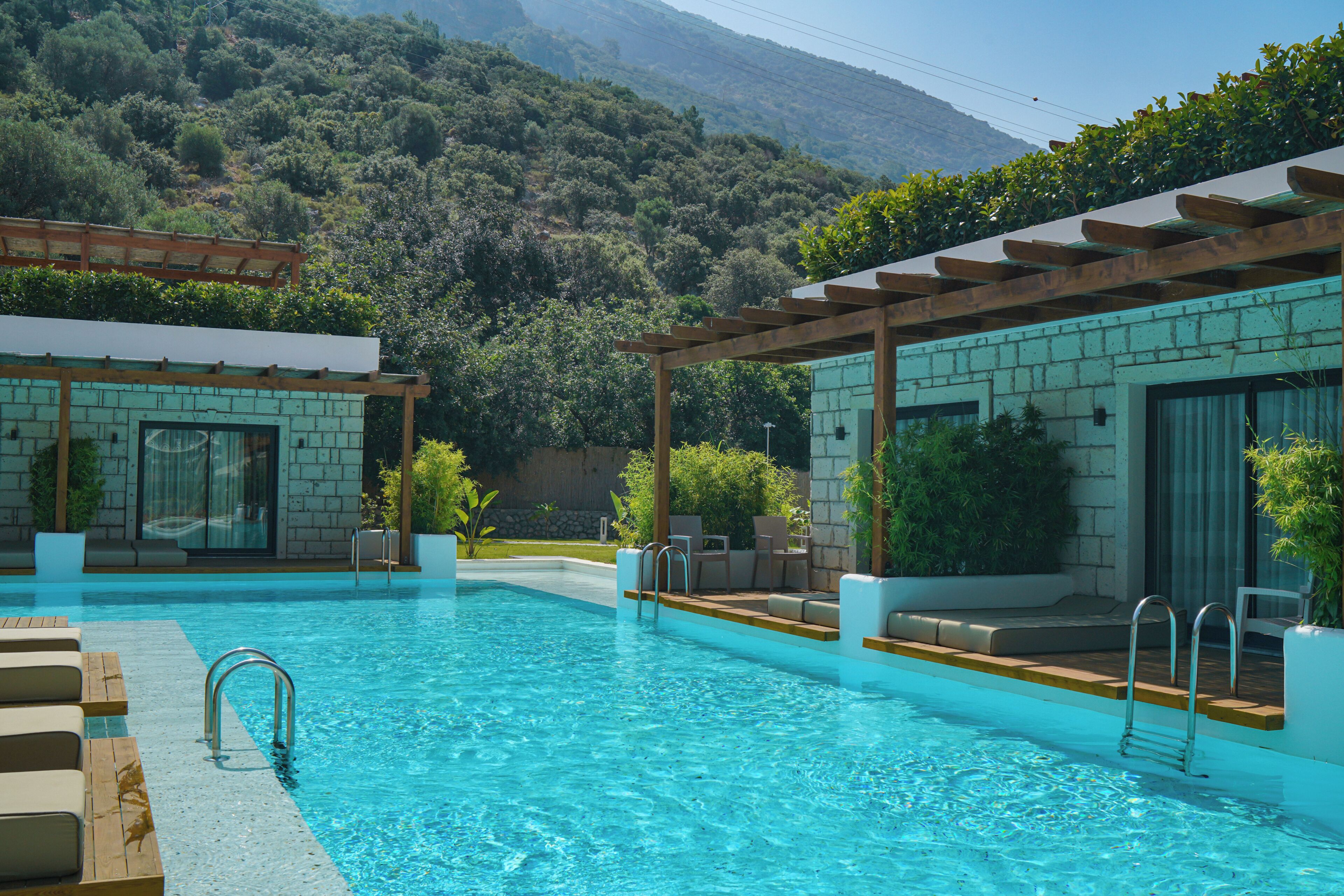 Una piscina con cubierta de madera, sillas de descanso y vistas a un paisaje montañoso.