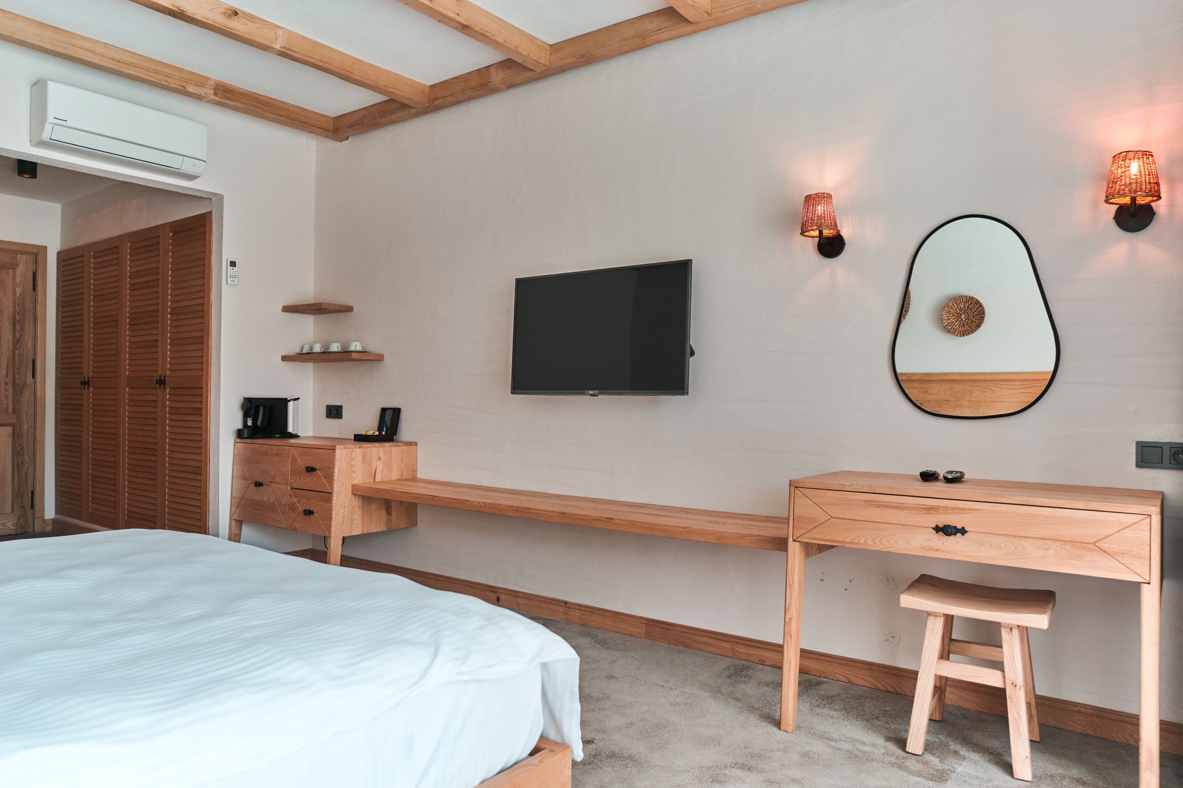 A bedroom with a bed, wooden desk, TV, and wall-mounted lights.