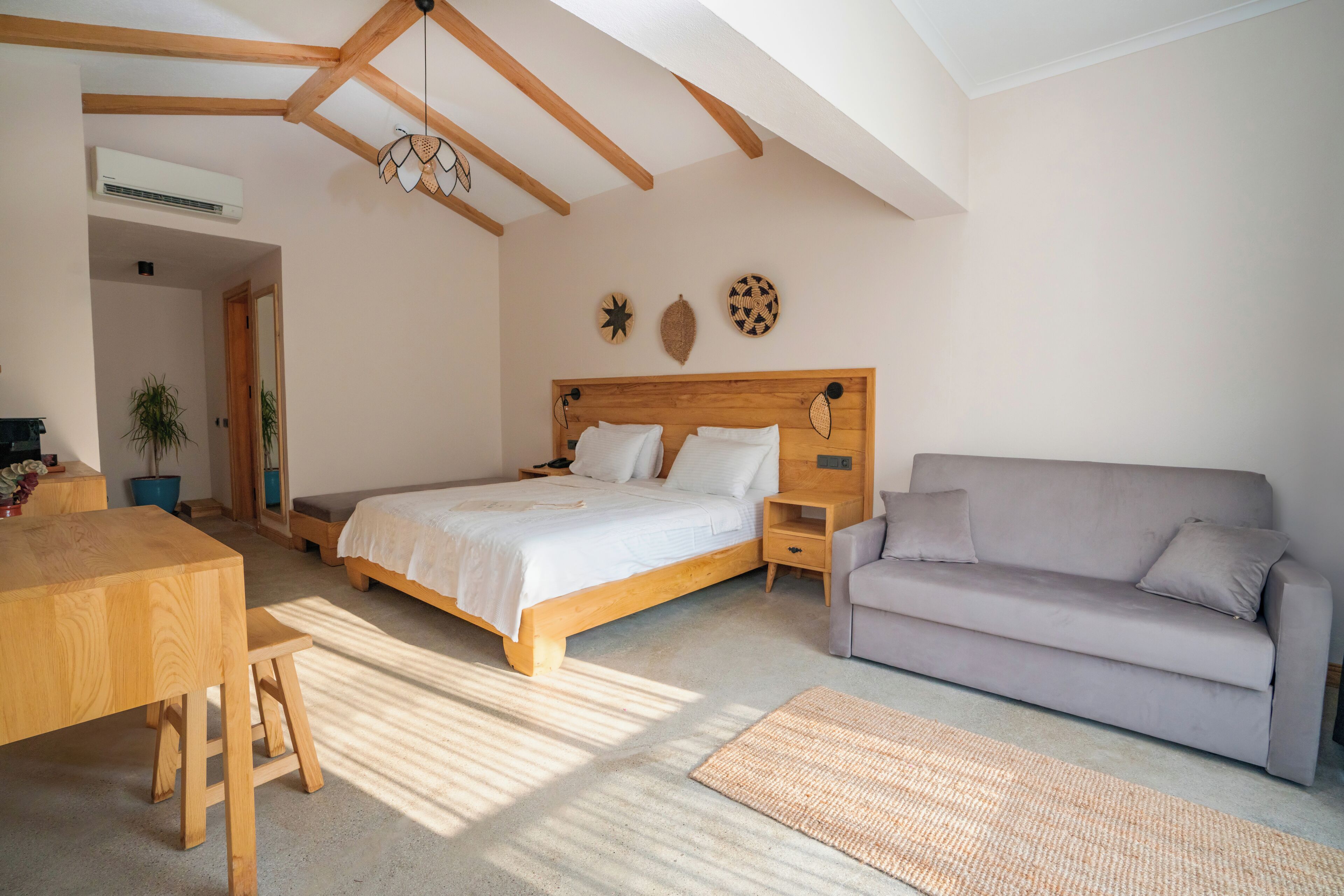 A bedroom with a wooden bed, a grey sofa, a wooden table, and a small stool.
