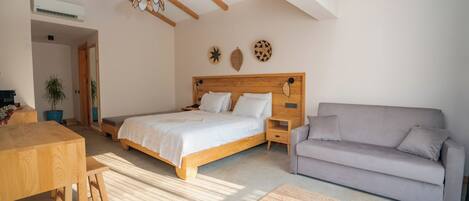 A bedroom with a wooden bed, a grey sofa, a wooden table, and a small stool.