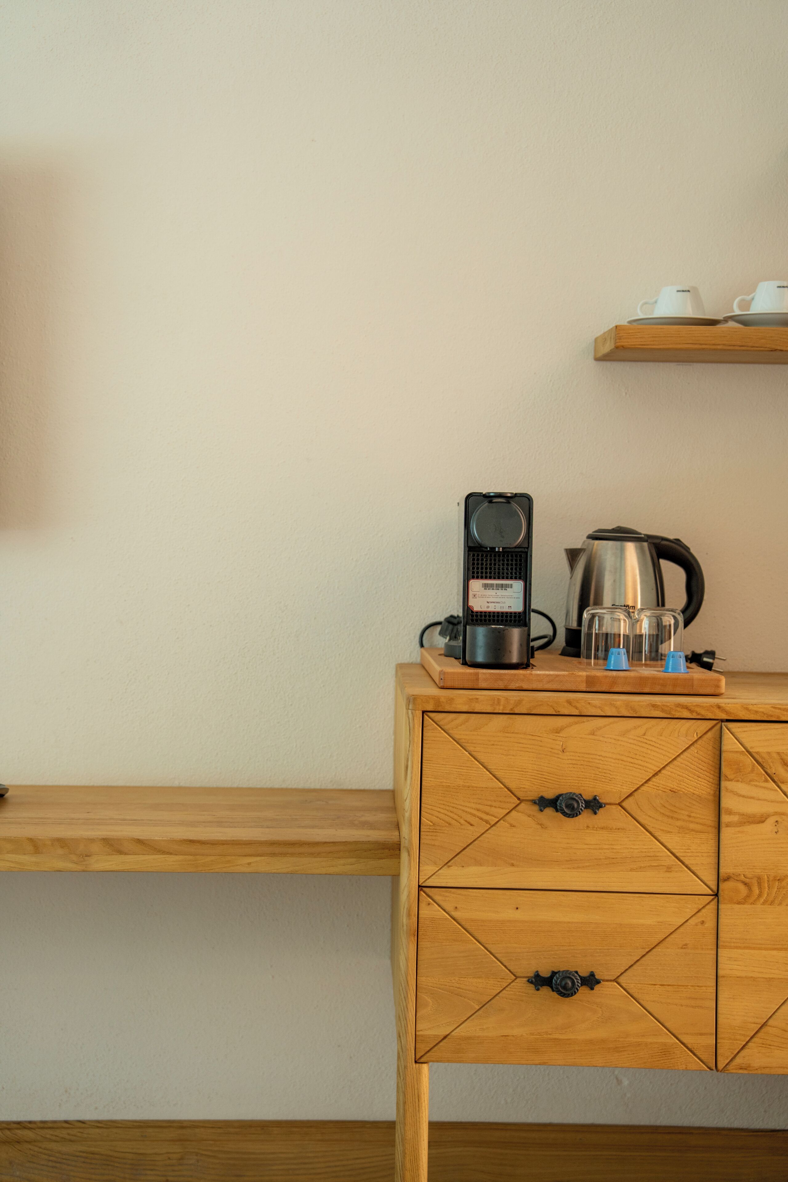 A wooden desk with a kettle, a coffee maker, and a cup on a shelf.