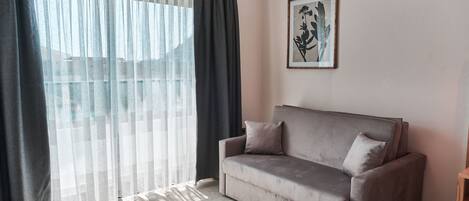 Una sala de estar con un sofá gris, un cuadro enmarcado en la pared y cortinas traslúcidas.