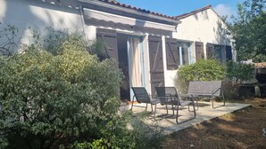 A building with a tiled roof, a covered patio with outdoor furniture, and a garden area with shrubs. - Large family house, large garden in an oyster site close to the beach (La perrotine)