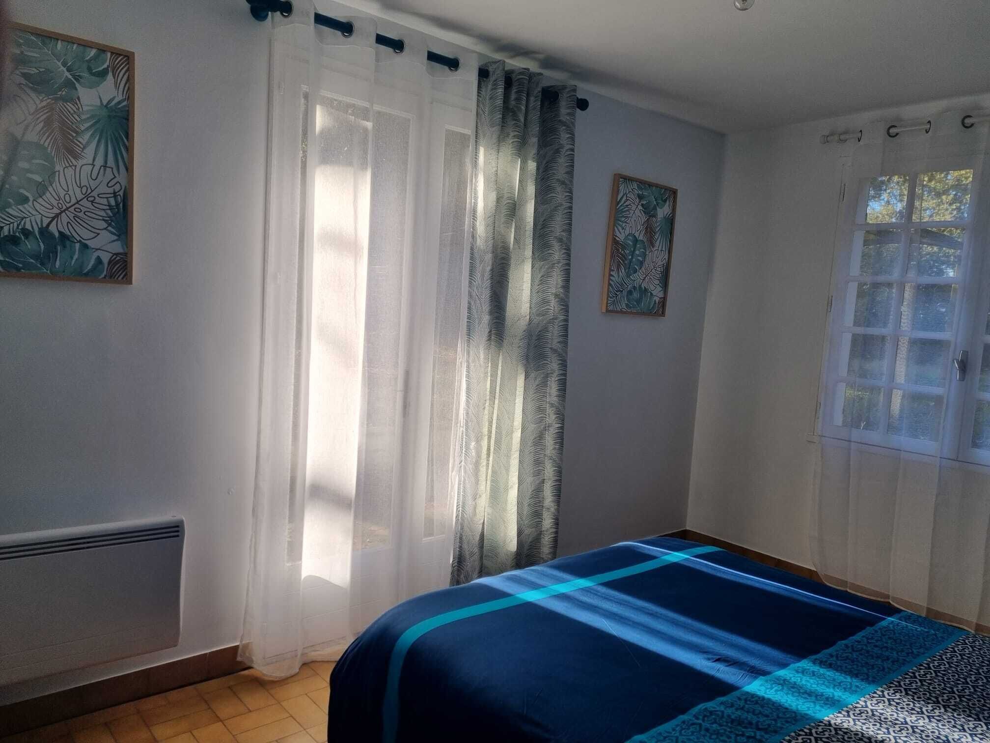 A bedroom with a bed, a window with curtains, and two wall-mounted pictures.