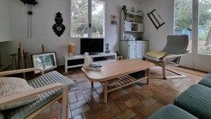 A living room with a television, a wooden coffee table, a sofa, and a chair. There are windows, a clock, and a shelf with various items. - Large family house, large garden in an oyster site close to the beach (La perrotine)