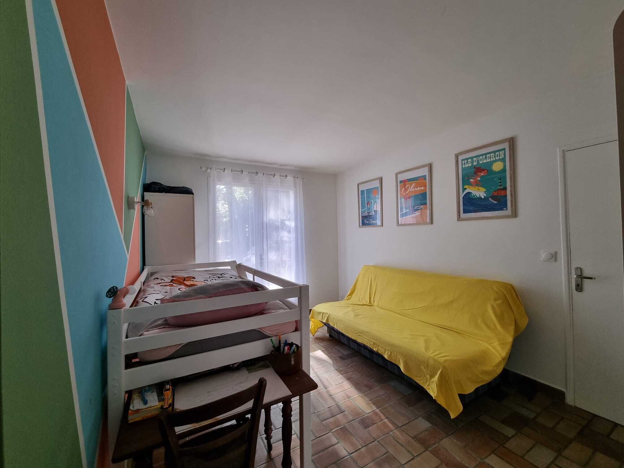 Quarto com cama de solteiro, sofá amarelo, escrivaninha com cadeira e janela com cortinas.