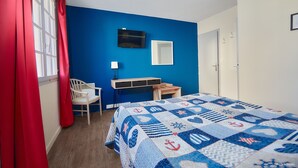 Een slaapkamer met een blauwe muur, een bed met een quilt met nautische motieven, een bureau, een stoel en een televisie aan de muur.