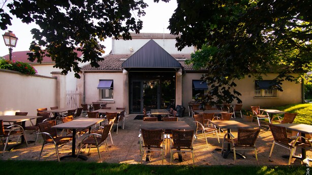 Een terras met meerdere tafels en stoelen, een overdekte ingang en een tuin.