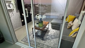 Un salon moderne doté d’une porte vitrée donnant sur un espace extérieur, d’un canapé avec des coussins, d’une table basse et d’une petite plante.