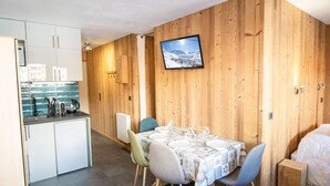 A compact room with a dining table set for four, a kitchenette, a bed, and a television mounted on the wooden wall. - Charming 2-Bedroom Apartment in Val Thorens - Sleeps 4, Renovated, Ski-In/Ski-Out! (Val Thorens)