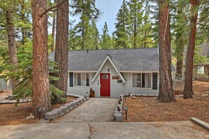 A lodge with a red door, surrounded by tall pine trees, and a gravel driveway leading to the entrance.