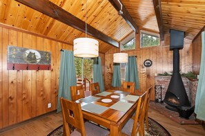 A wooden interior with a dining table, chairs, a fireplace, and a sign welcoming guests.