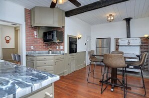 A kitchen with a marble countertop, a stove, and a refrigerator. There are two bar stools and a clock on the wall.