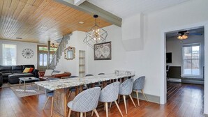 Una sala de estar amplia con techo de madera, una zona de comedor con mesa de mármol y una escalera que sube a otro nivel.