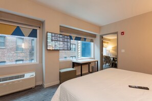 A hotel room with a bed, a desk, and a window overlooking a brick building.