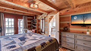 A cozy log cabin bedroom with a large bed, a dresser, and a television displaying a moonlit tree. - Bears Valley #171 (Sevierville)