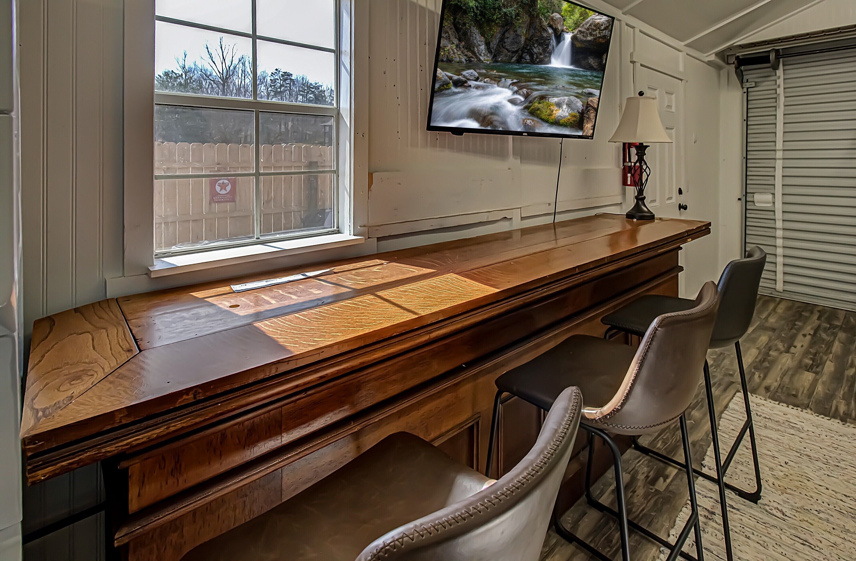 A bar area with a wooden countertop, a television mounted above it, and two bar stools.