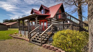 A rustic cabin with a red front door, wooden deck, and a staircase leading to a balcony. - Bears Valley #171 (Sevierville)