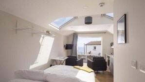 A bedroom with a skylight, a bed, a desk, and a seating area with chairs. - Stylish Boatshed with Sea Views, Private Parking (Gorran Haven)