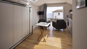 A compact living space with a skylight, a dining area, a TV, and a view of the outside. - Stylish Boatshed with Sea Views, Private Parking (Gorran Haven)