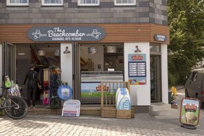 Een winkel met strandthema, met een bord dat "The Beachcomber" vermeldt, en dat strandartikelen, cadeaus en ijs aanbiedt.