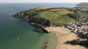 An aerial view of a coastal town with a beach, rocky coastline, and buildings. - Stylish Boatshed with Sea Views, Private Parking (Gorran Haven)