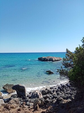 A rocky shoreline with clear blue water and distant rocky formations.