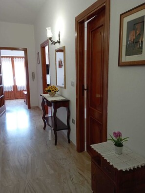 Um corredor com porta de madeira, espelho emoldurado e pequena mesa com um vaso de flores.