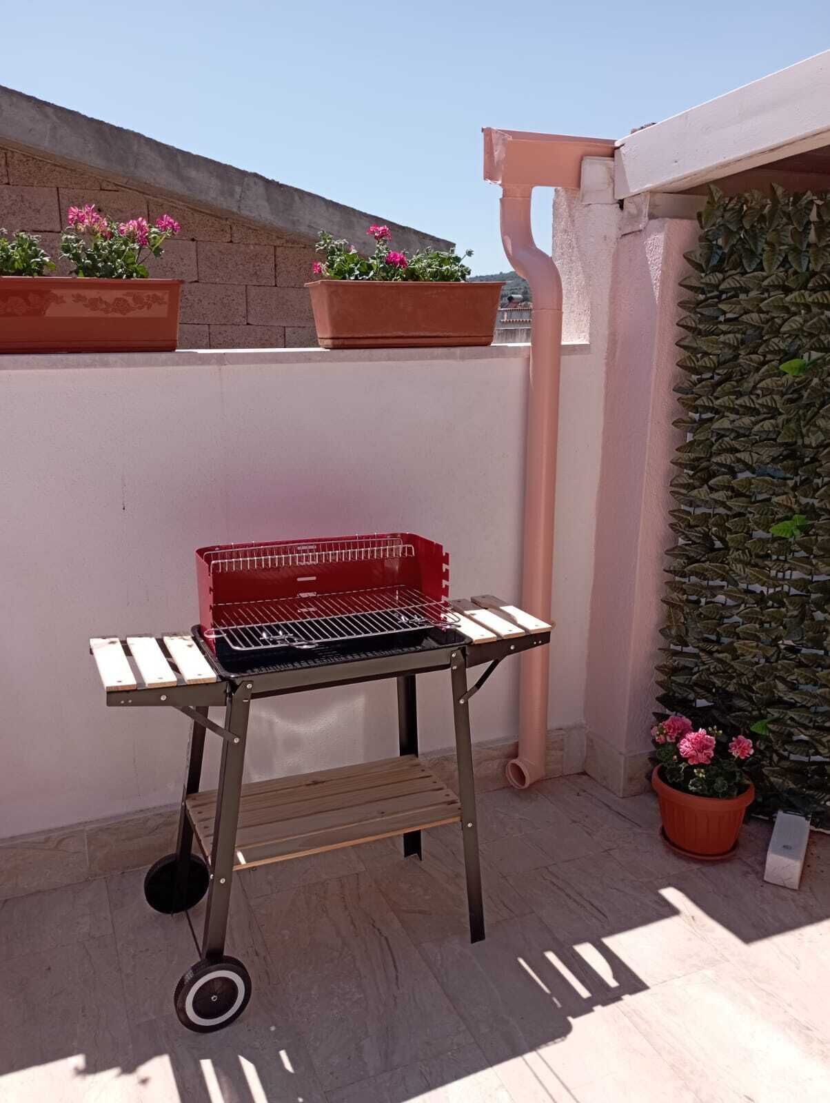 A portable barbecue grill on a balcony with potted plants and a wall-mounted plant wall.