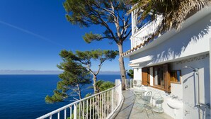 Un balcon donnant sur la mer, avec une vue imprenable, une balustrade blanche et un petit espace extérieur aménagé avec des chaises et une table.