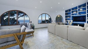 Un salon moderne doté de grandes fenêtres en arc de cercle, d’un canapé beige, d’un banc en bois et d’une étagère bleue agrémentée d’objets décoratifs.