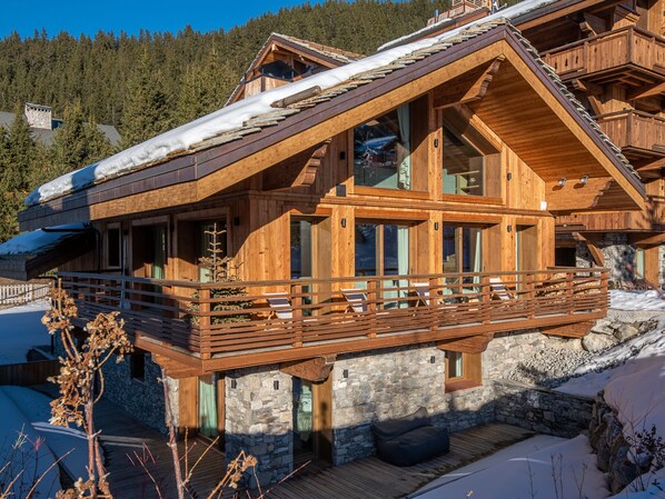 A wooden chalet with a balcony, stone foundation, and large windows. - Luxury Chalet with 7 Bedrooms, Spa Access, and Stunning Mountain Views (Méribel)
