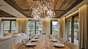 A dining area with a wooden table set for a meal, large windows, and a chandelier. - Luxury Chalet with 7 Bedrooms, Spa Access, and Stunning Mountain Views (Méribel)