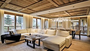 A spacious living room with a wooden ceiling, large windows, a chandelier, and a sofa set. - Luxury Chalet with 7 Bedrooms, Spa Access, and Stunning Mountain Views (Méribel)