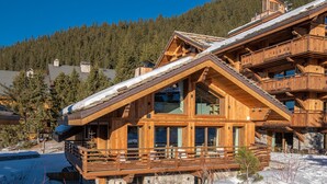 A wooden chalet with a balcony, surrounded by snow and trees. - Luxury Chalet with 7 Bedrooms, Spa Access, and Stunning Mountain Views (Méribel)