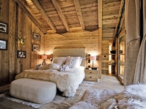 Una habitación acogedora de madera con una cama, una mesita de noche y un reposapiés cubierto de piel.