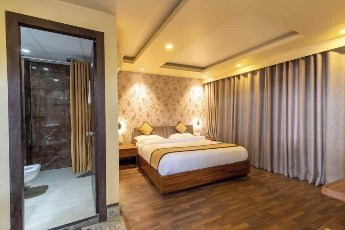 Una habitación de hotel moderna con piso de madera, una cama grande con cabecera, cabina de ducha de vidrio y vista a la ciudad.