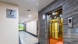 Un pasillo interior con pared de mármol, un letrero que indica el séptimo piso y un ascensor con pantalla digital.
