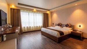 Habitación de hotel con una cama grande, mesitas de noche, un escritorio con silla, televisión y una ventana con cortinas.